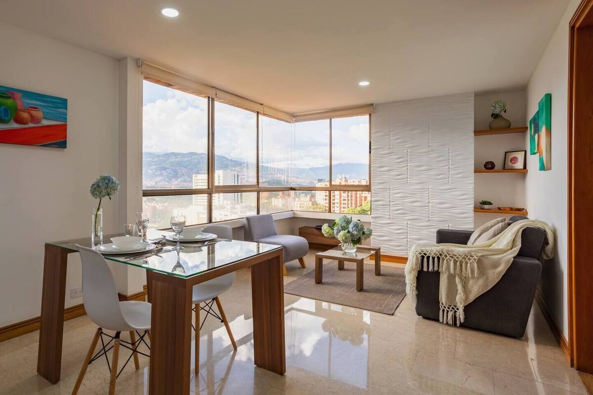 A modern living room with a dining area, large windows, and a city view.