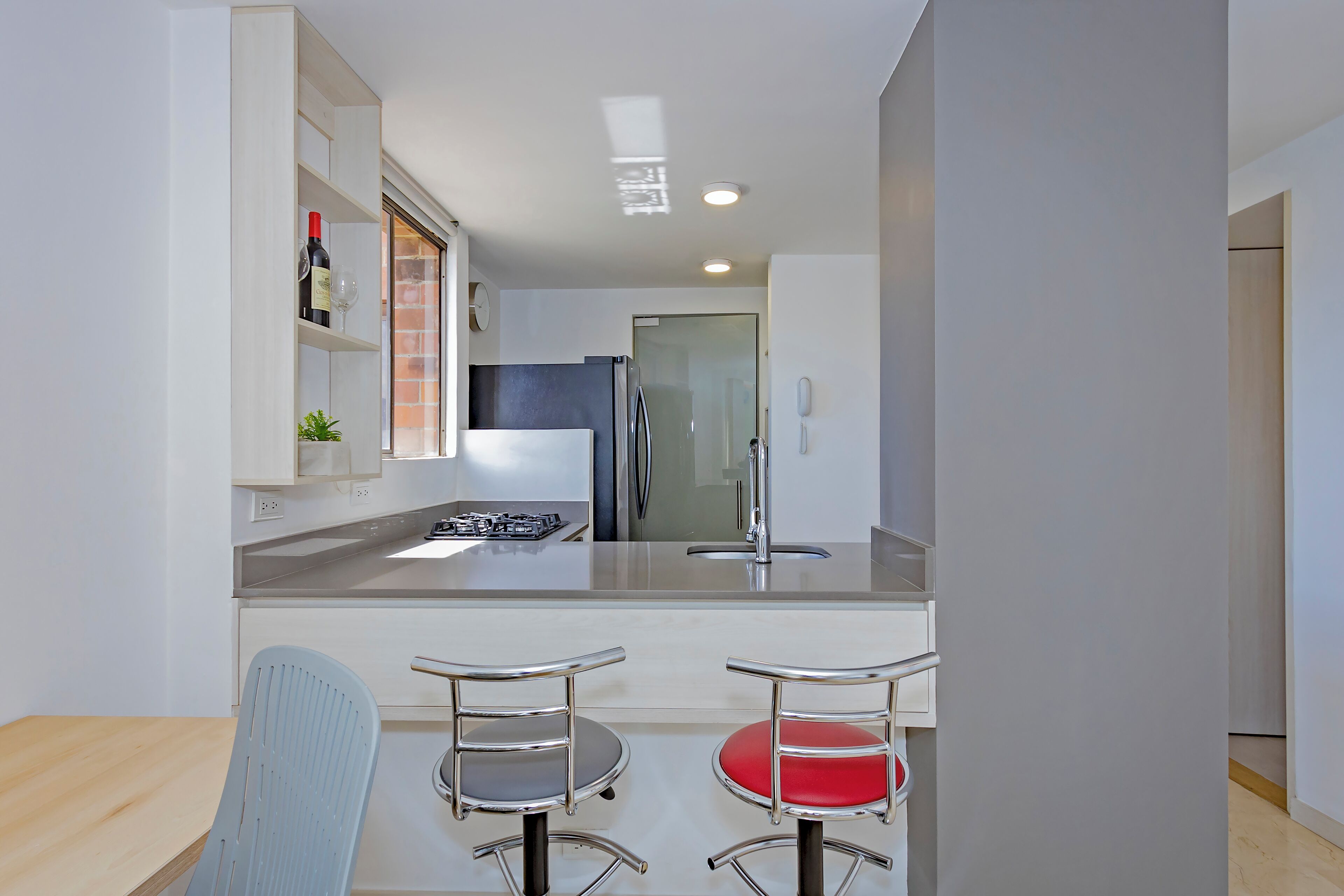 A modern kitchen with a central island, stainless steel appliances, and two bar stools with red cushions.