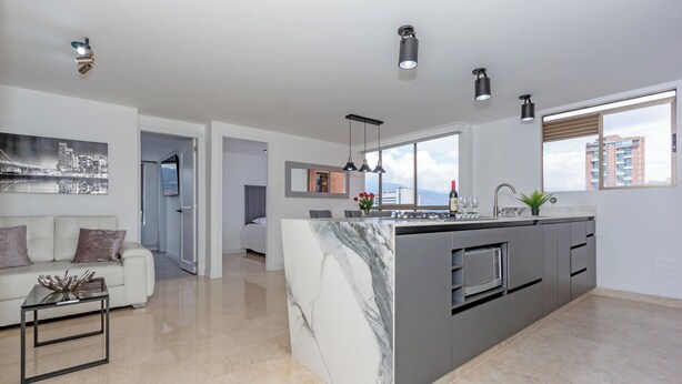 Cocina moderna con isla de mármol, iluminación colgante y vistas de la ciudad a través de amplias ventanas.