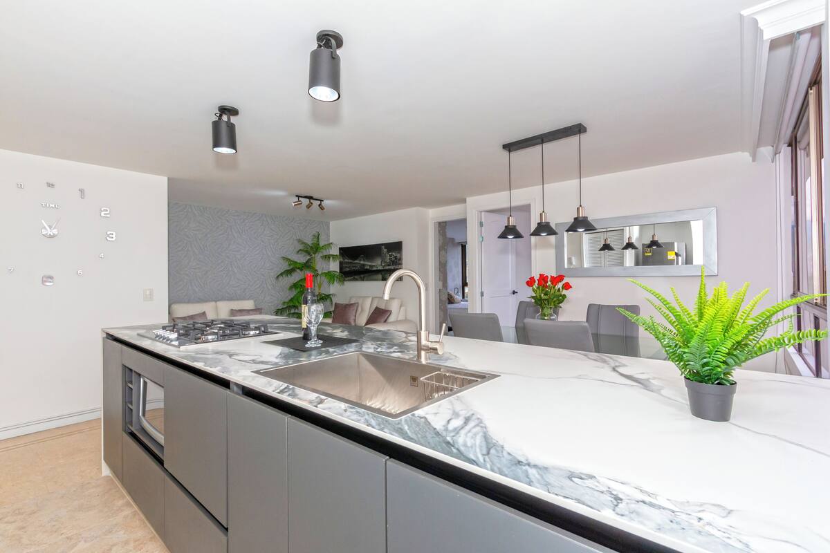 A modern kitchen with a marble countertop, stainless steel sink, and pendant lighting.