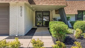 A modern two-story house with a brick exterior, a garage door, and a well-maintained front yard with various shrubs and a pathway leading to the entrance. - Tulsa Twilight Terrace@StFrancis (Tulsa)