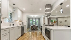 A modern kitchen with white cabinetry, a central island, and a dining area with a table and chairs. - Tulsa Twilight Terrace@StFrancis (Tulsa)