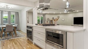 A modern kitchen with a central island, built-in oven, and a dining area with a table and chairs. - Tulsa Twilight Terrace@StFrancis (Tulsa)