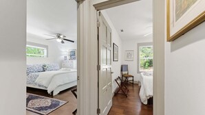 Een slaapkamer met een bed, een plafondventilator, een raam en een deur naar een badkamer met een handdoekhouder en een stoel.
