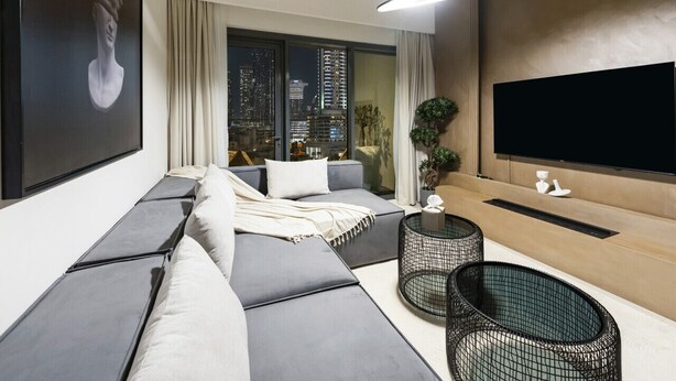Ein modernes Wohnzimmer mit einer großzügigen Eckcouch, einem flachbildfernseher an der Wand und Blick auf die Stadt durch große Fenster.