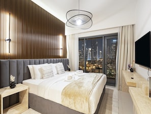 Une chambre d’hôtel moderne dotée d’un grand lit, d’une vue sur la ville, d’un téléviseur à écran plat et d’un élégant luminaire suspendu.