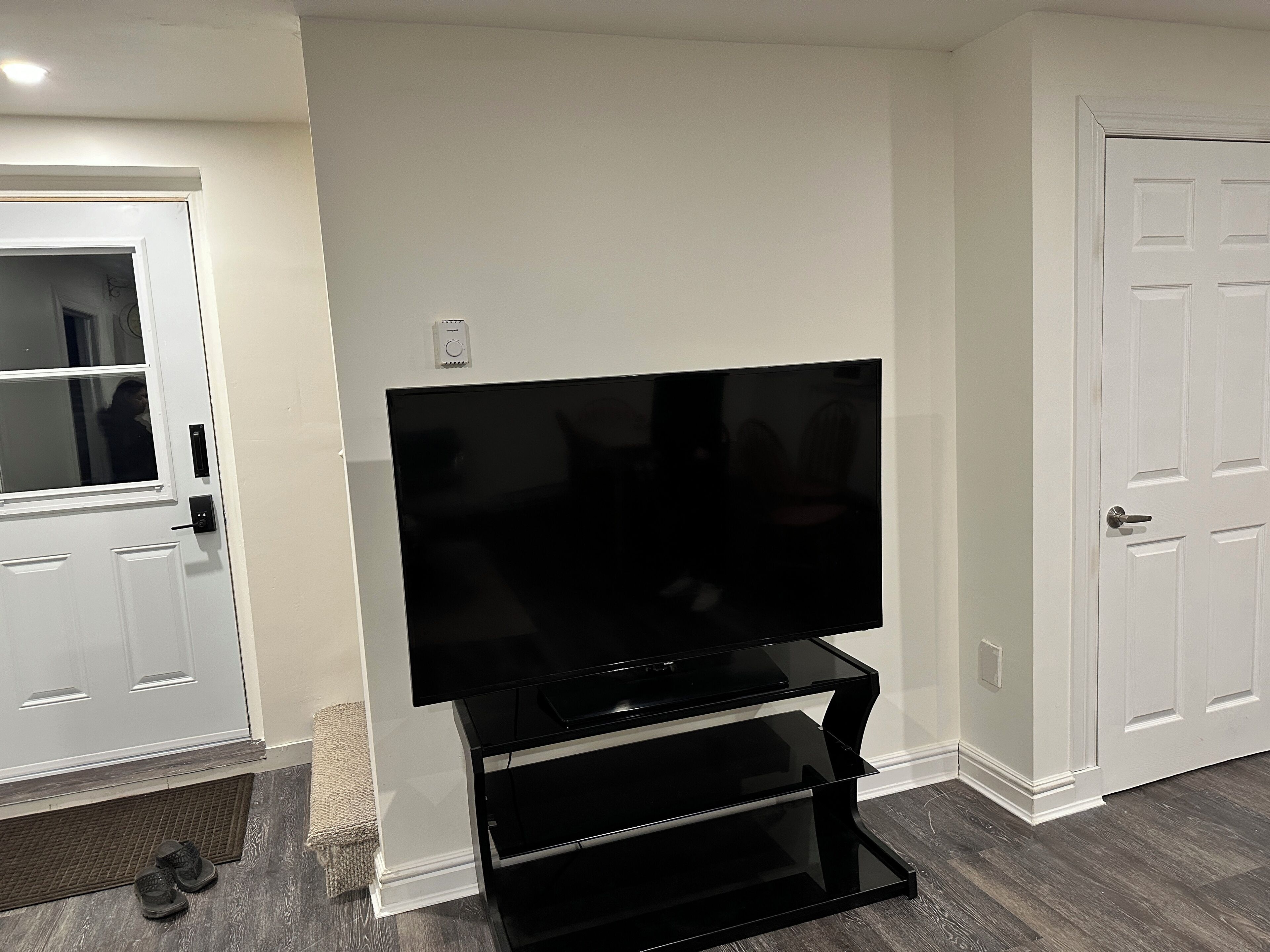 Een kamer met een flatscreentelevisie op een zwart voetstuk, een witte deur en een witte muur.