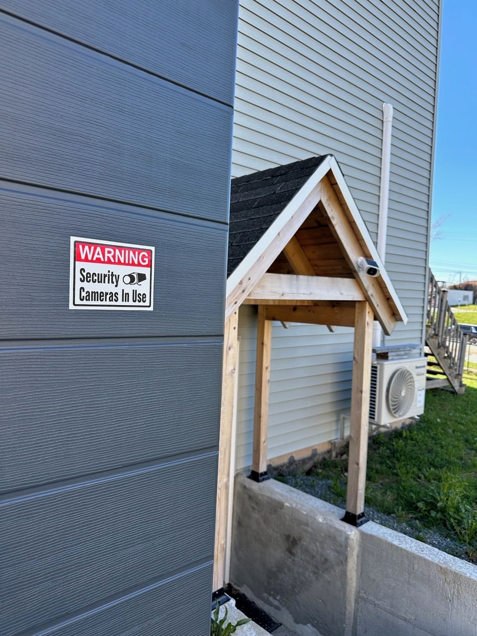A house with a security warning sign, a wooden structure resembling a doghouse, and an air conditioning unit.