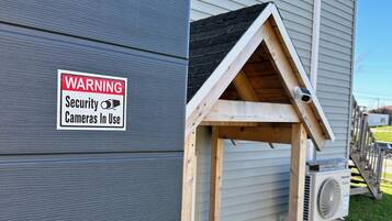 A house with a security warning sign, a wooden structure resembling a doghouse, and an air conditioning unit.