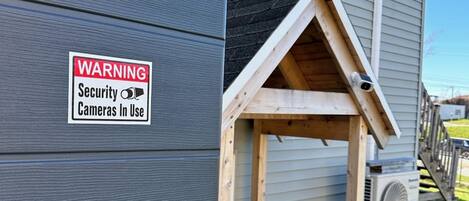 A house with a security warning sign, a wooden structure resembling a doghouse, and an air conditioning unit.