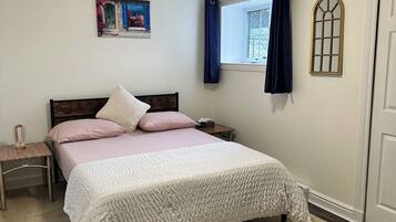 Une chambre à coucher comprenant un lit, une table de chevet, une fenêtre avec des rideaux, un tableau accroché au mur et une porte.