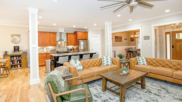 A spacious living room with a large sofa, a coffee table, and a dining area with a kitchen in the background. - Epic 13 Bed Golf Vacation - Chipping Inn (Pinehurst)