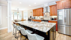A modern kitchen with a large island, wooden cabinets, stainless steel appliances, and bar stools. - Epic 13 Bed Golf Vacation - Chipping Inn (Pinehurst)