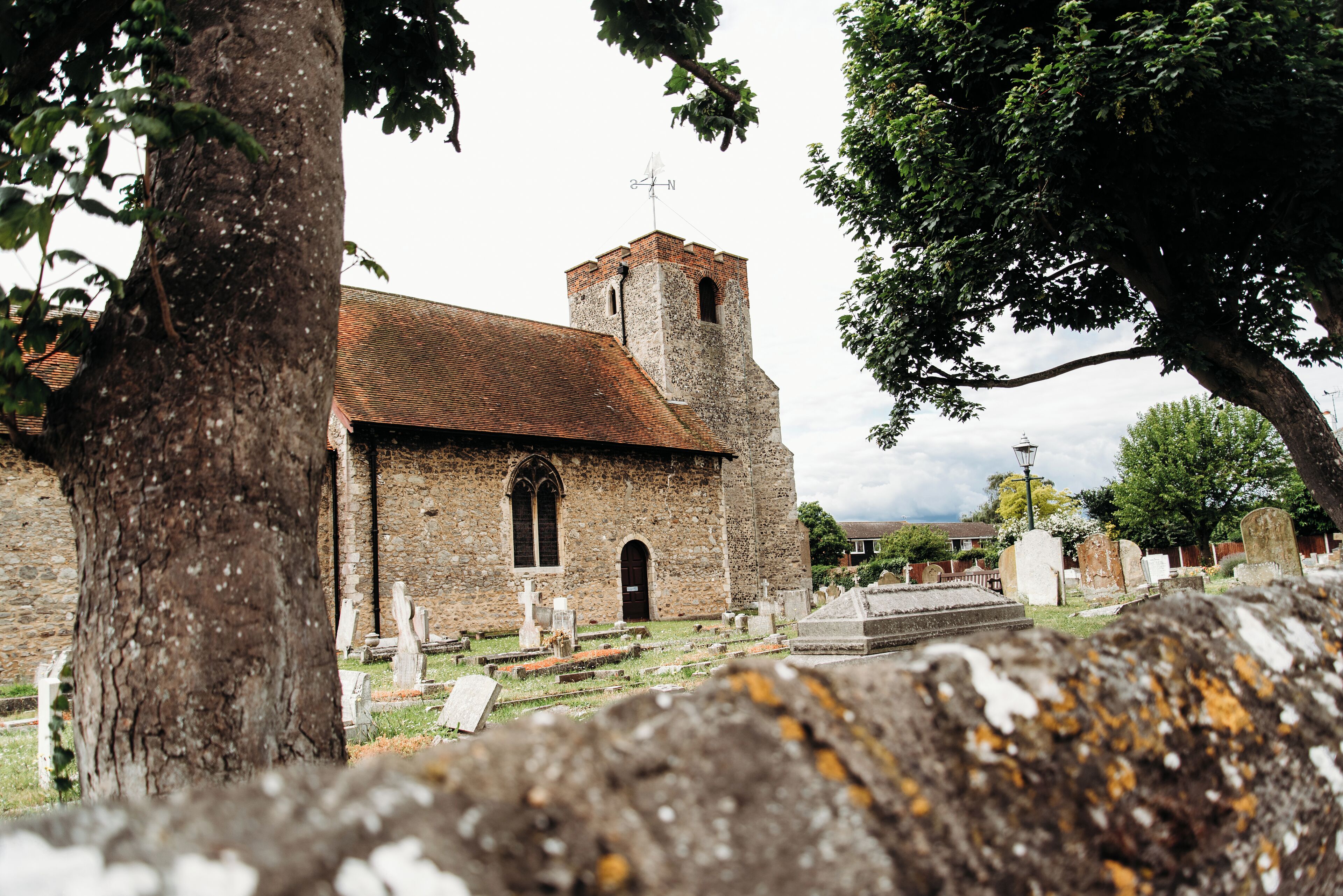 Une église dotée d’un clocher, entourée d’arbres et de pierres tombales.
