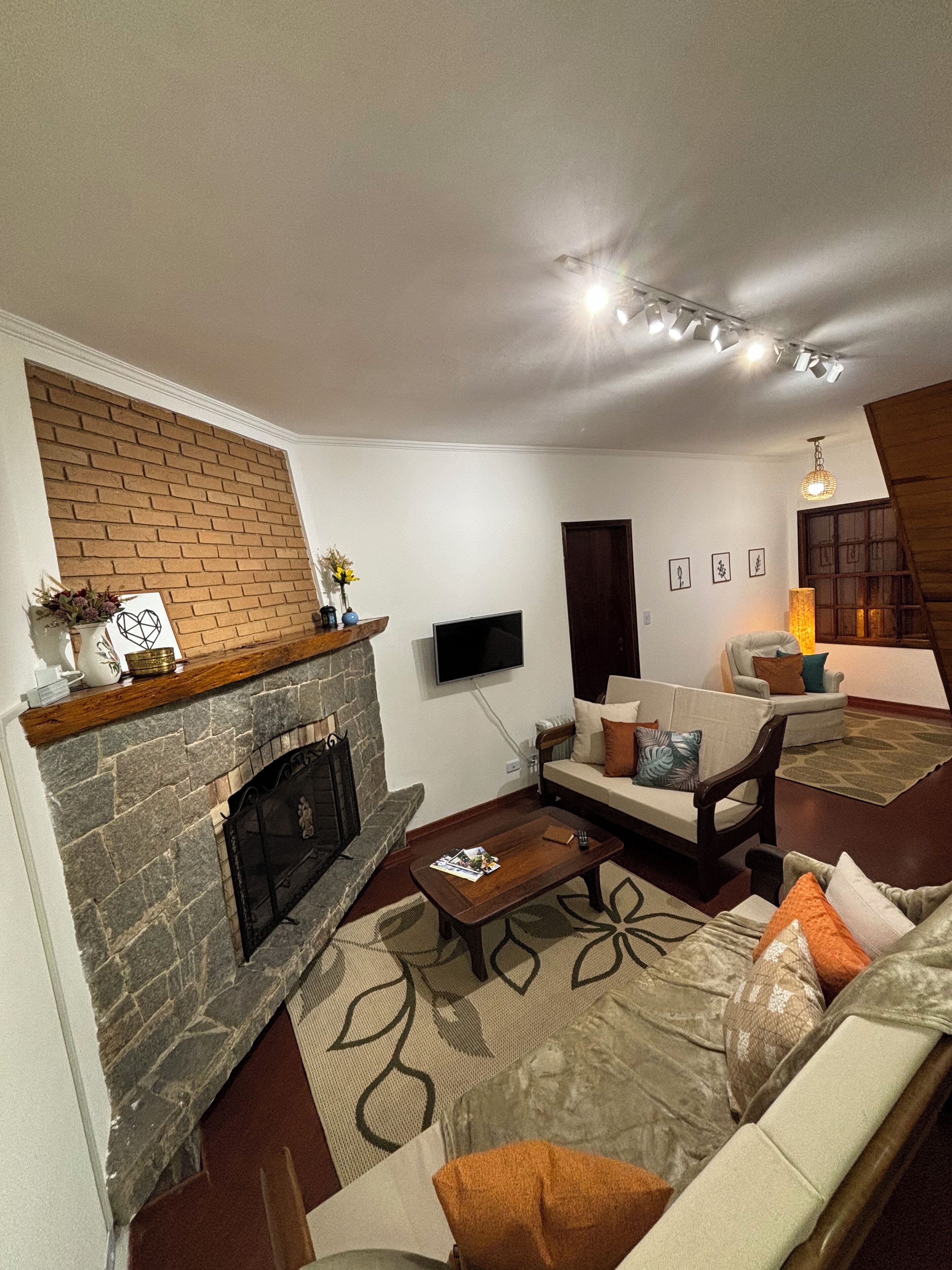 Ein Wohnzimmer mit Kamin aus Backstein, einer Couch, einem Couchtisch und einem an der Wand befestigten Fernseher.