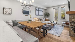 Una sala de estar moderna con una mesa de comedor de madera, un sofá gris y una chimenea.