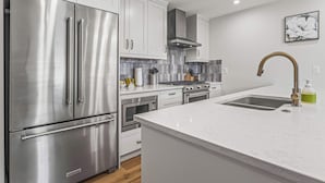 Una cocina moderna con electrodomésticos de acero inoxidable, armarios blancos, una encimera de mármol y un lavaplatos de acero inoxidable.