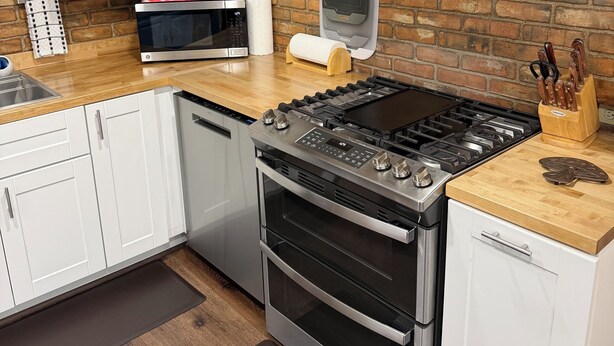 Cocina moderna con gabinetes blancos, estufa de acero inoxidable y pared de ladrillo.