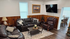 Una sala de estar con un sofá de cuero, un sillón reclinable, una mesa de centro y un televisor.