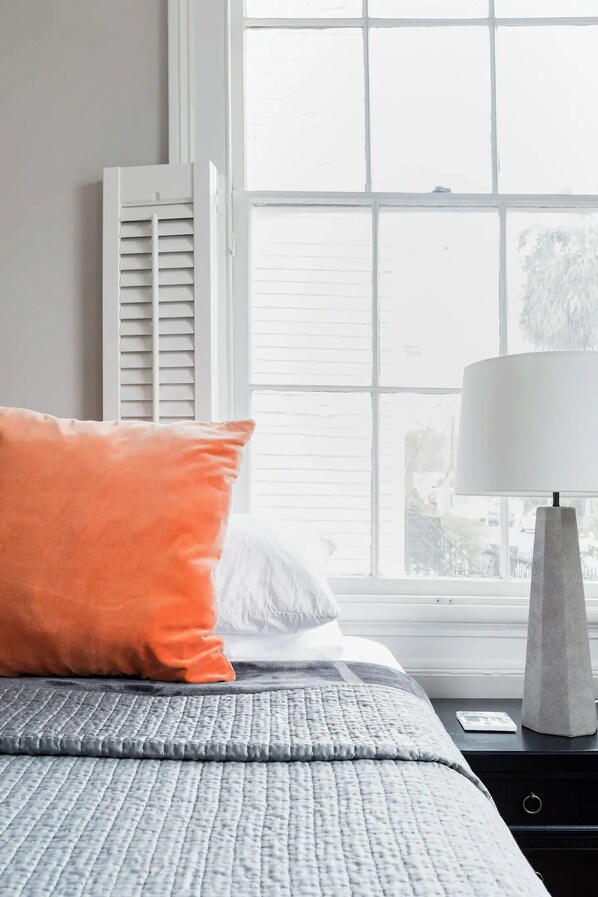 A bedroom with a bed, a window with blinds, a lamp, and a nightstand.