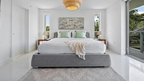 Ein modernes Schlafzimmer mit einem großen Bett, einer Pendelleuchte aus Rattan und Blick auf Grün durch das Fenster.