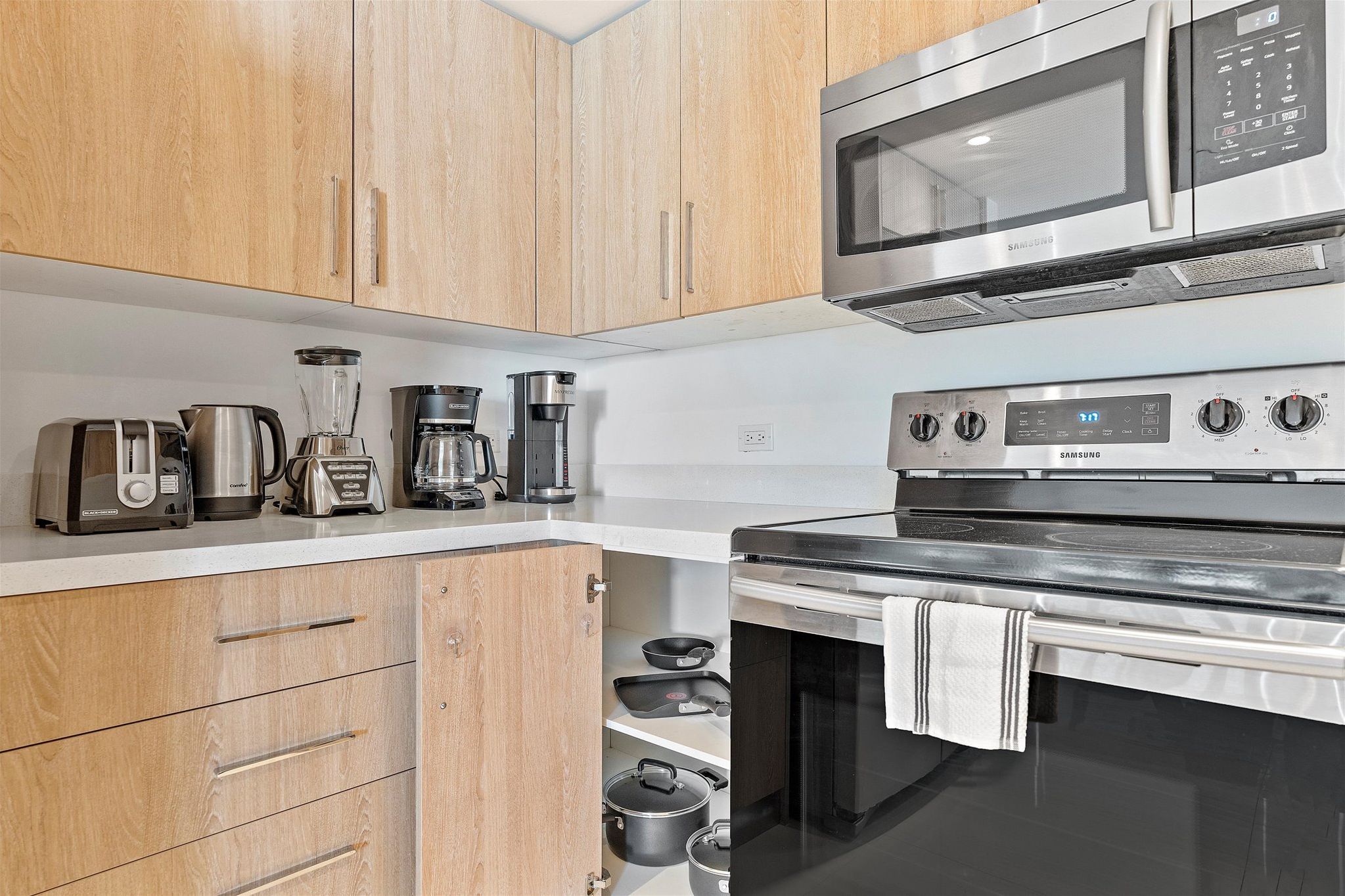 A modern kitchen with wooden cabinets, a stainless steel microwave, a built-in oven, and various appliances like a toaster and coffee maker.