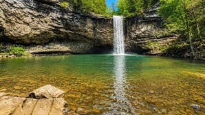 Uma cascata despencando em uma piscina límpida, rodeada por penhascos rochosos.