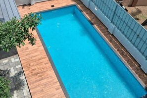 A rectangular swimming pool with a wooden deck surrounding it. - Grand Residency & Resort (Varkala)