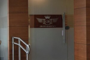 Puerta con un cartel que dice 'GRAND RESIDENCY' y una barandilla de metal a la izquierda.