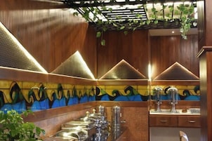 Interior de un restaurante con una larga barra, plantas colgantes y una pared decorativa con diseño de olas.