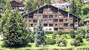 A multi-story building with a complex architectural design, surrounded by lush greenery and a lake.