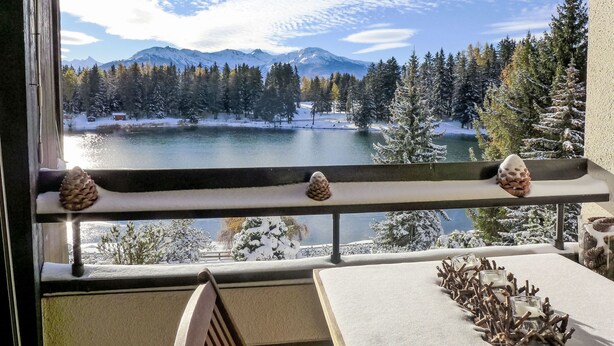A balcony with a view of a snowy lake and mountains.