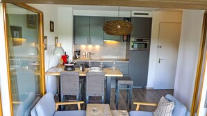 A compact kitchen with modern appliances, a dining area with two chairs and a table, and a small seating area with a sofa and two chairs.