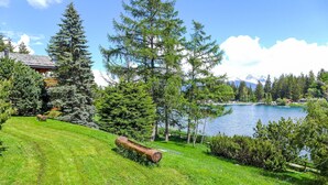 A grassy area with a wooden log, a lake, and a house in the background.