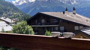 Een houten berghut met een balkon, houten leuningen en twee witte kopjes op de leuning.