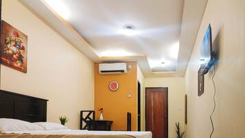 A hotel room with a bed, a desk, a chair, a clock, an air conditioning unit, a TV, and a door.