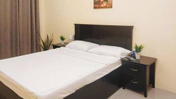 A hotel room with a bed, a nightstand, a small table, and a potted plant.