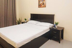 Une chambre d’hôtel avec un lit, une table de chevet, une petite table et une plante en pot.