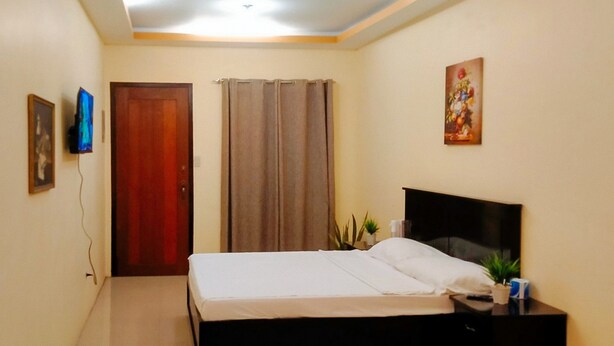 A bedroom with a bed, a nightstand, a television, and a door. - Reddoorz @ Kbl Transient Inn San Fernando (Bacolor)