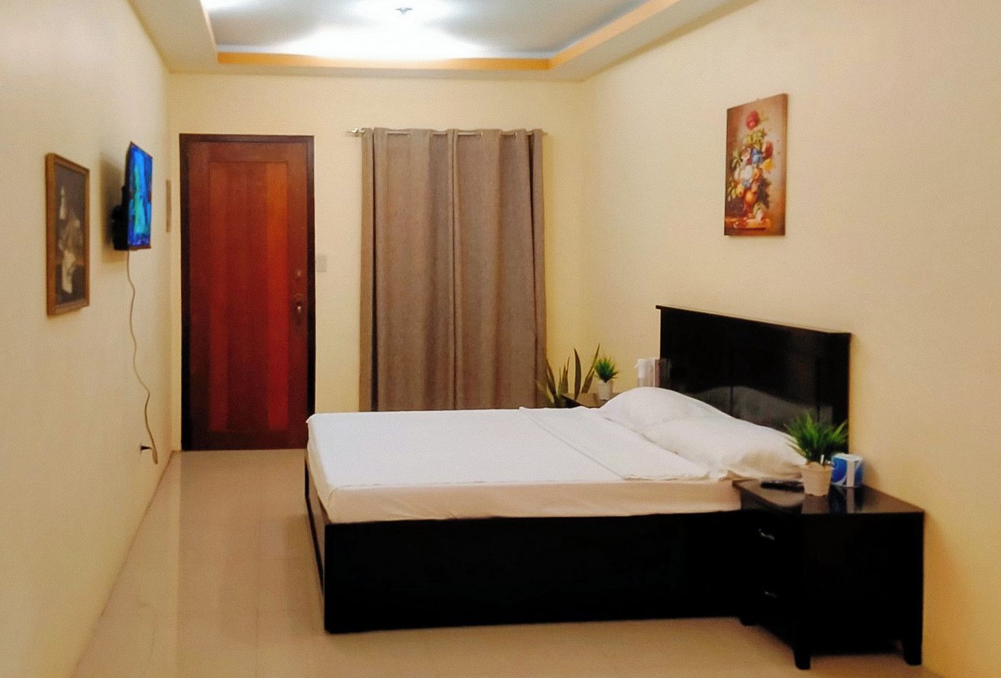 A bedroom with a bed, a nightstand, a TV, a door, and a painting on the wall.