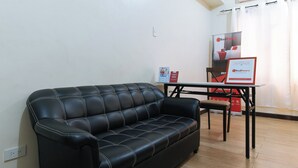 A black leather sofa, a small table, and a RedDoorz sign in a room with white walls and wooden flooring. - Reddoorz @ Kbl Transient Inn San Fernando (Bacolor)