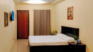 A bedroom with a bed, a nightstand, a TV, a door, and a painting on the wall. - Reddoorz @ Kbl Transient Inn San Fernando (Bacolor)