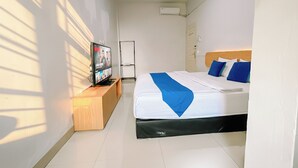 Una habitación de hotel con cama, televisor sobre un soporte de madera, unidad de aire acondicionado blanca y una puerta con manija.