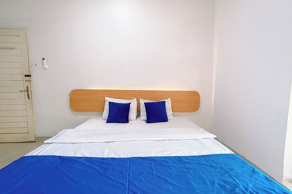 A single bed with a wooden headboard, white bedding, and two blue pillows.