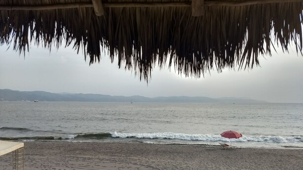 Ein Strand mit einer strohgedeckten Struktur, einem roten Sonnenschirm und einem Stuhl.