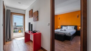 Ein Hotelzimmer mit Balkon, einem roten Schreibtisch, einem Bett mit zwei Kissen und einer orangefarbenen Akzentwand.