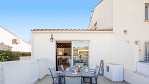 A patio with a table set for four, surrounded by chairs, and a sliding glass door leading to an indoor area. - Villa 12 Cassin by Interhome (Canet-Plage)