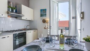 Moderni keittiö, jossa on valkoiset kaapit, kaasuliesi ja uuni. Ruokapöytä on katettu lautasilla, laseilla ja viinipullolla.