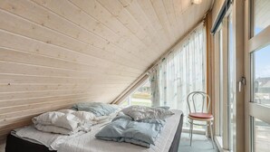 A small, cozy bedroom with a sloped ceiling, a bed with multiple pillows, a chair, and a large window offering a view of the outdoors. - Pet friendly home in Thisted with sauna (Thisted)
