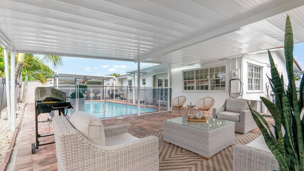 A covered outdoor area with a pool, wicker furniture, and a grill. - Stunning Home with a HEATED POOL 4 miles to the beach! (Pompano Beach)
